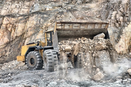 Wheel loader machine unloading rocks in the open-mine of iron ore