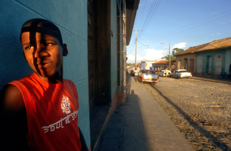 Boy portrait and colourful houses and people in a street scene. Classic American car parked on a street with traditional,in the background, Trinidad, Cuba, West Indies, Central Americaのeditorial素材