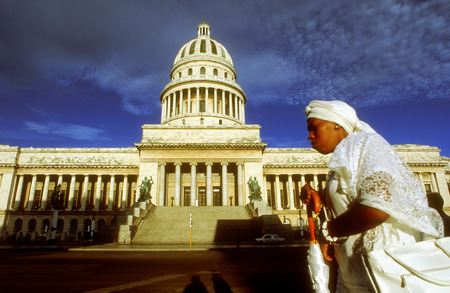 Woman santera passing the Capitolio Nacional, Havana, Cuba. SanterÃ­a, also known as Regla de OchÃ¡ or La Regla de LucumÃ­ is a syncretic religion of Caribbean origin which developed in the Spanish Empire among West African slaves. SanterÃ­a is influencedのeditorial素材
