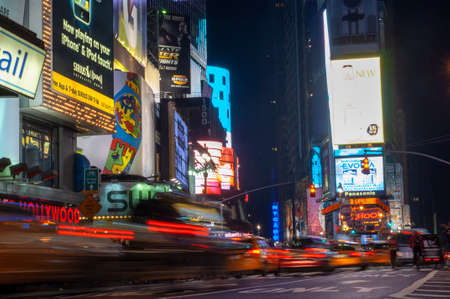 Bright neon signage flashes over crowds and taxi traffic zooming past Times Square the venue of the city's famous New.のeditorial素材