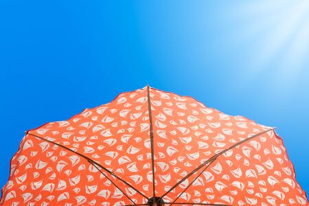 bright orange bright orange beach umbrella against a clear blue sky lit by the rays of the sun,...