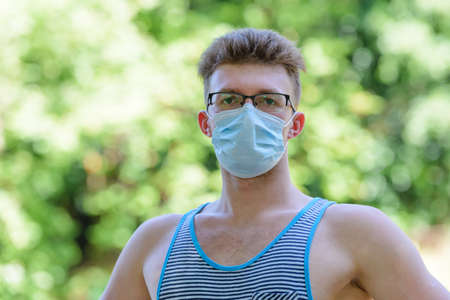portrait of a young man with a medical mask on his face on a natural green backgroundの写真素材