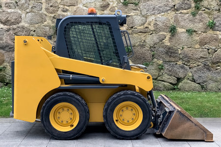 small yellow industrial street tractor for road works with a bucket parked in the street, close-up
