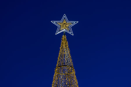 glowing Christmas tree with a star on the top against the background of the night blue skyの写真素材