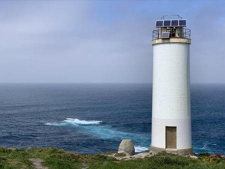 A lighthouse is on a rocky shoreline. The water is calm and the sky is cloudy. The lighthouse is white and tallの写真素材