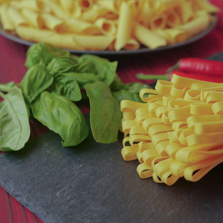 Tagliatelle with basil on a black stone board in the background a plate of garganelliの写真素材