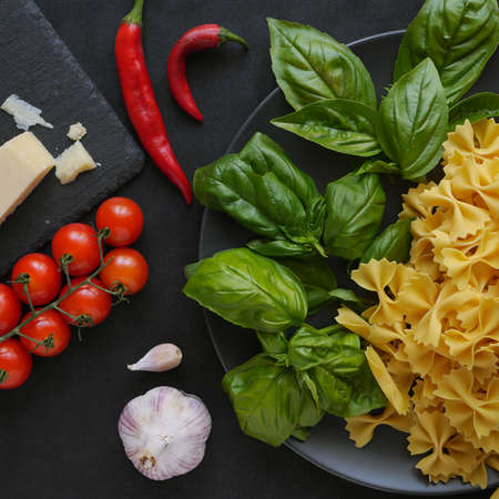 Pasta farfalle and basil on a plate standing on a black background next to vegetables and spicesの写真素材