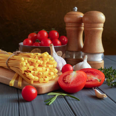 Tagliatelle pasta is tied with a cord on a wooden board around vegetables, spices and herbsの写真素材