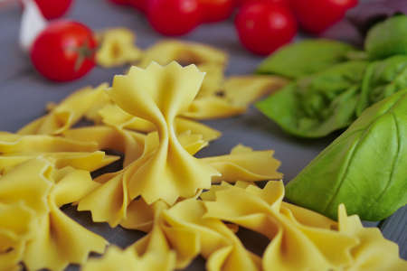 Homemade farfalle close up on a background of cherry tomatoes and basilの写真素材