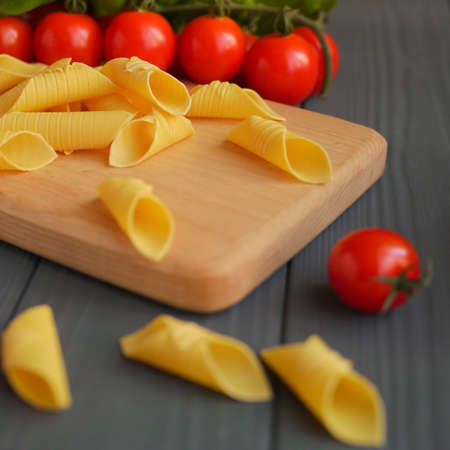 Garganelli pasta on the kitchen board behind the tomatoesの写真素材