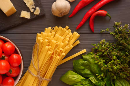 Tagliatelle pasta on the table surrounded by spicy herbs and vegetablesの写真素材