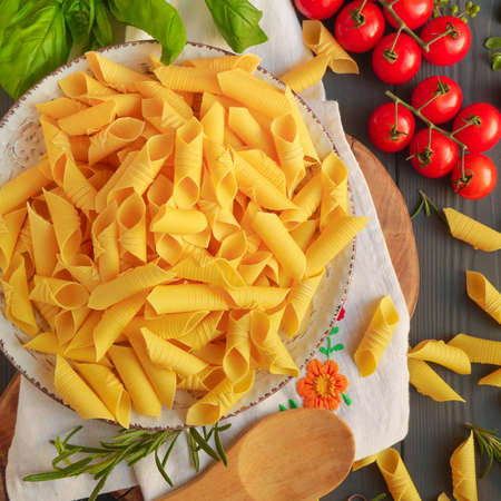 Garganelli pasta on a plate next to tomatoes and rosemaryの写真素材