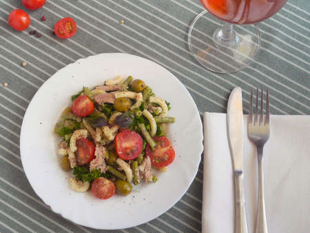 Pasta and tomato salad on a white plate with a glass of wineの写真素材