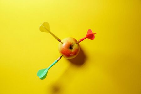 Yellow arrow dart hitting the target apple isolated on yellow background. Minimal idea food and fruit conceptの写真素材