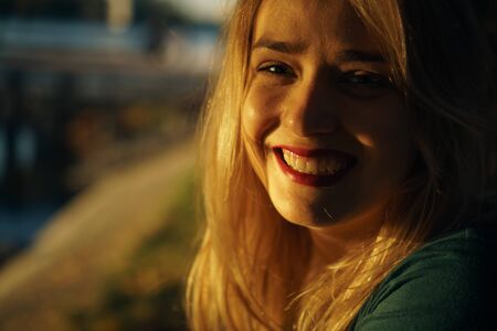 Autumn portrait of young happy smiling girl with red lips at sunsetの写真素材