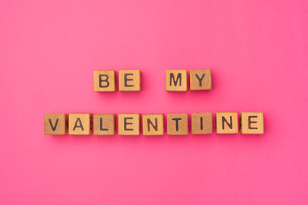 Wooden cubes with the phrase Be My Valentine on an empty colorful pink background. Words of love are made of letters from wood for Valentine's Day and for your girlfriend, boyfriend, wife, husband greeting romantic postcard. Flat lay, top viewの写真素材