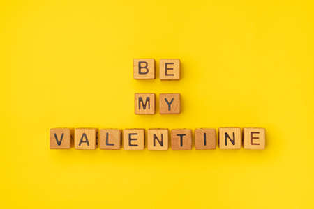 Wooden cubes with the phrase Be My Valentine on an empty colorful yellow background. Words of love are made of letters from wood for Valentine's Day and for your girlfriend, boyfriend, wife, husband greeting romantic postcard. Flat lay, top viewの写真素材