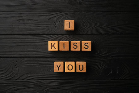 Wooden cubes with the phrase I Kiss You on a black background - a wooden table. Words of kiss are made of letters from wood for your girlfriend, boyfriend, wife, husband, for Valentine's Day greeting romantic postcard. Flat lay, top viewの写真素材