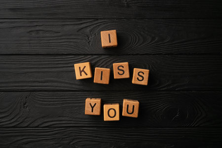 Wooden cubes with the phrase I Kiss You on a black background - a wooden table. Words of kiss are made of letters from wood for your girlfriend, boyfriend, wife, husband, for Valentine's Day greeting romantic postcard. Flat lay, top viewの写真素材