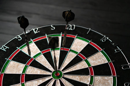 Three darts hit the dartboard. Lucky - one of the darts hits the bulls eye. The concept of winning and luck. Close-up, angled viewの写真素材