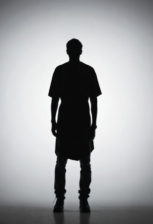 A man stands upright in profile, creating a striking silhouette against a soft, illuminated backdrop. His posture exudes confidence in this minimalist black and white portrayal.の素材