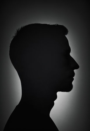 A solitary figure stands in profile, the silhouette of a man highlighted against a gentle glow, suggesting a reflective moment in an intimate setting during nighttime.の素材