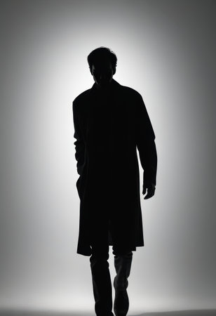 A solitary figure draped in a long coat strides forward, creating a striking black silhouette against a gentle white backdrop, evoking feelings of mystery and contemplation.の素材