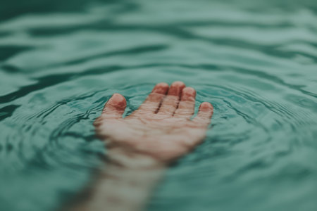 A mans hand and arm gently float above calm waters, creating ripples that enhance the serene atmosphere. Soft tones and a pastel color palette complement the soothing vibe.の素材