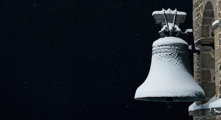 An ancient church bell, completely blanketed in a thick layer of white snow, is illuminated against a deep black sky as light snow falls on a cold, peaceful evening.の素材