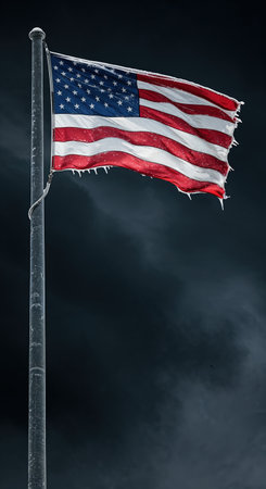 A weathered flag with red and white stripes and a blue field of stars, adorned with ice, flutters on a pole against an ominous, dark, cloudy backdrop.の素材