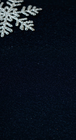 A deep luxurious navy blue textured background provides ample copy space, subtly accented by a glistening silver snowflake decoration in the upper corner.の素材