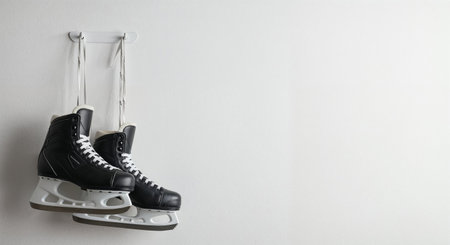 Two clean ice hockey skates are suspended by their white laces on a simple hook, positioned against a pristine, even lit white background, evoking a sense of calm and readiness.の素材