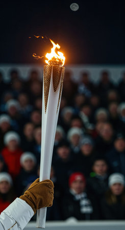 The dramatic orange flame of a ceremonial torch illuminates the night, held by a person in a brown glove, with spectators gathered in the soft-focused background under a clear moonlit sky.の素材