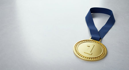 This close-up view captures a gleaming first-place gold medal with its rich blue ribbon resting on a subtle gray background, offering a significant room for text or graphics.の素材
