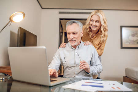 A man working from home, his wife standing next to himの写真素材