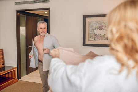 A man a nd a woman getting dressed in a hotel roomの写真素材