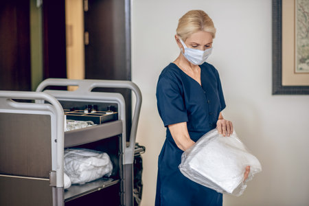 Service woman in a protective mask with a trolley carrying clean towelsの写真素材