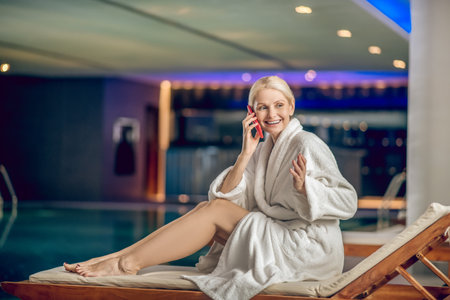 Pretty woman in a white robe talking on the phone while being in a spa centerの写真素材