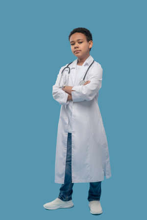 Serious boy in white coat with arms folded on chestの写真素材