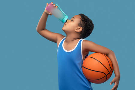 Boy with ball drinking water from sports bottleの写真素材