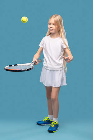 Smiling girl tossing ball with tennis racketの写真素材