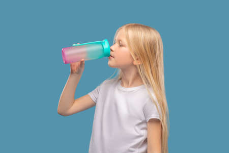 Girl with drooping eyelids drinking from sports bottleの写真素材