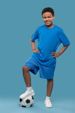 Joyful boy in sportswear holding ball with footの写真素材