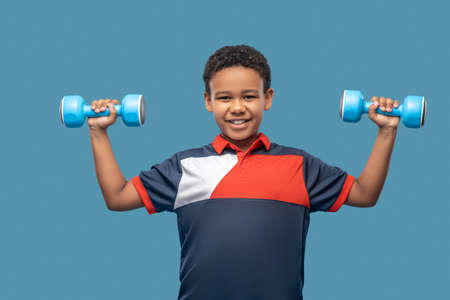 Happy dark skinned boy lifting dumbbells in handsの写真素材