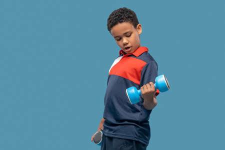 Dark skinned boy doing strength exercise with dumbbellsの写真素材