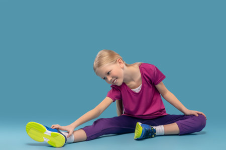 Girl sitting on floor bending over to outstretched legの写真素材