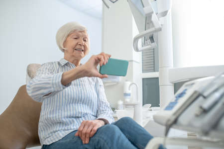 Gray-haired woman making selfie after tooth restoration and looking contentedの写真素材