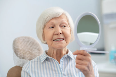 Senior woman looking in the mirror after visiting dentists officeの写真素材