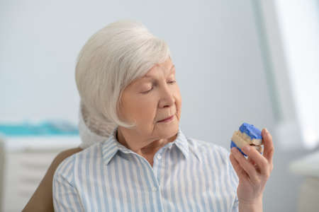 Senior woman holding a denture and looking thoughtful