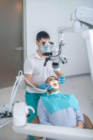 Male dental surgeon working with patient and using optical medical instrumentの写真素材
